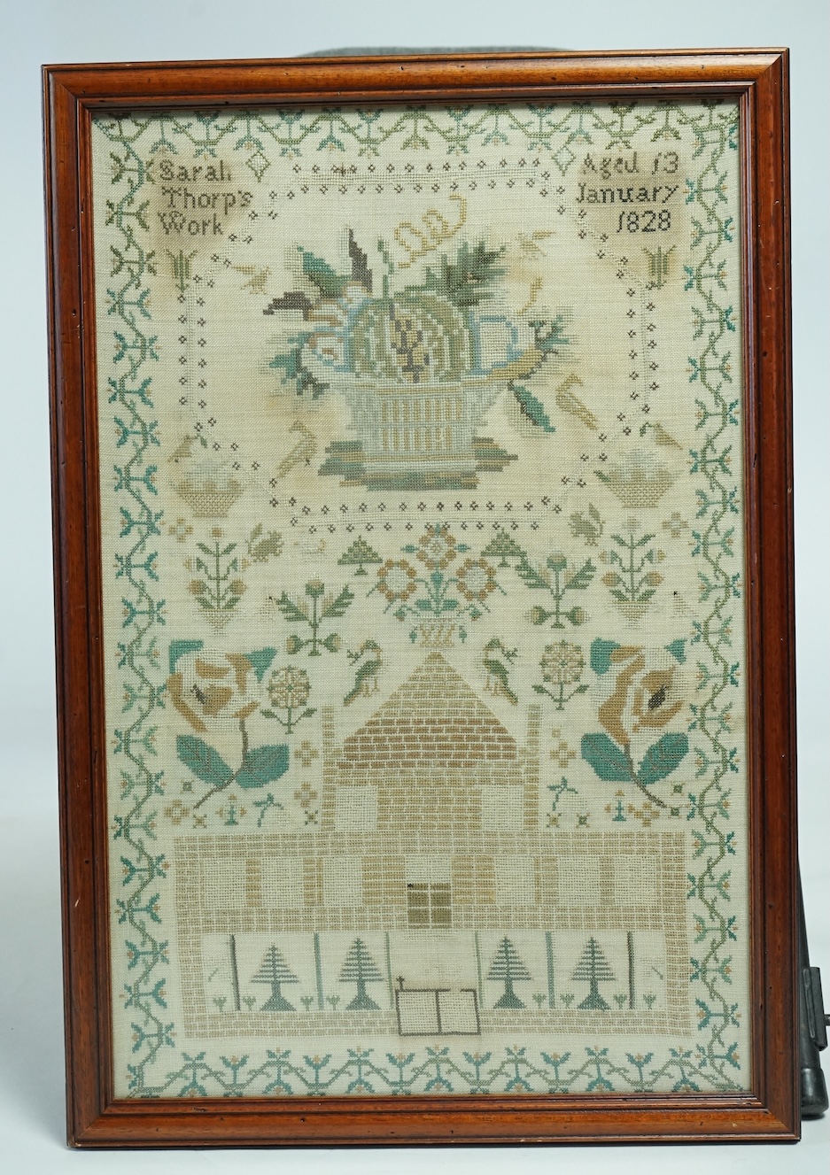 A framed 1828 large cross stitch sampler embroidered by Sarah Thorp aged 13 years. Worked with large motifs of flowers, baskets of fruit, peacocks, squirrels, trees, a large house and border. 40cm wide x 60cm high. Condi